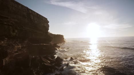 epic aerial drone view of a cliff at sunset over a village near lisbon while the waves splash against the rocks and in slow motion