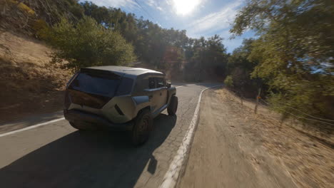 toma de drones fpv de la vista trasera de un vehículo deportivo utilitario resistente en la carretera que pasa a través de árboles sombreados en la luz del día de verano para anuncios comerciales de automóviles, con hermosas tomas cinematográficas de primer plano