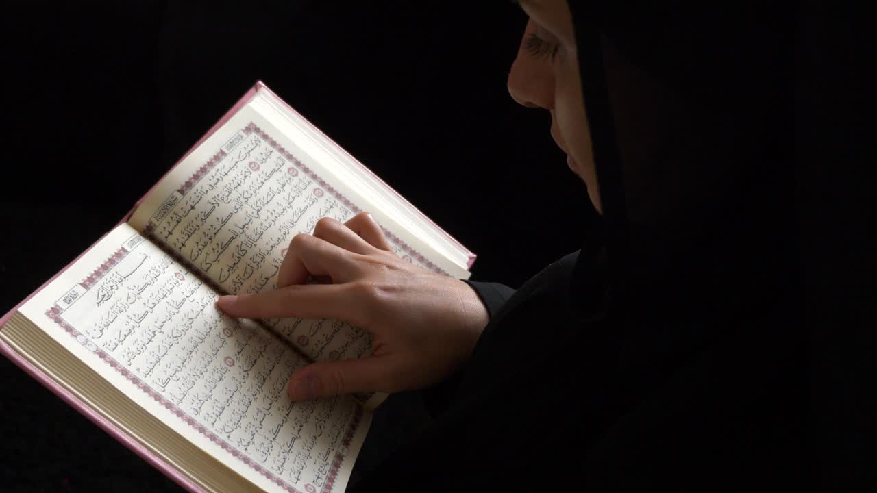히자브를 입은 무슬림 여성이 꾸란을 들고 몇 구절을 읽고 있는 측면 사진