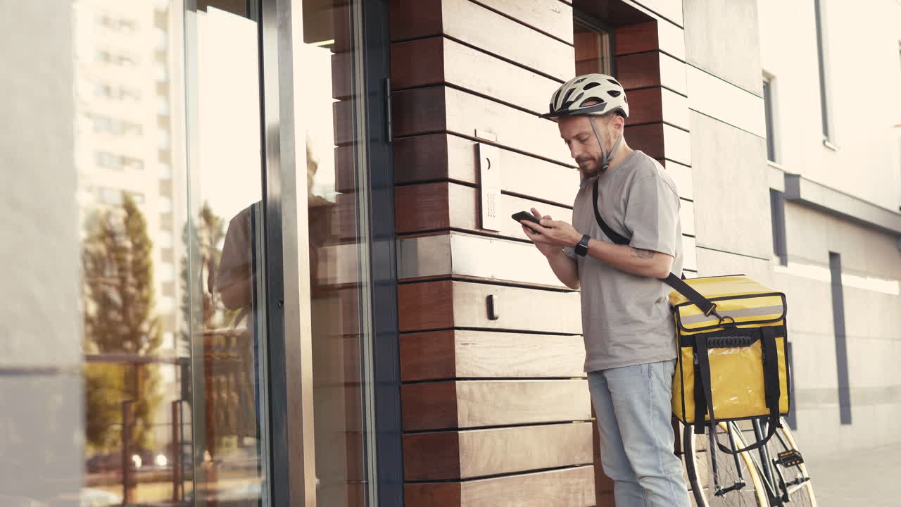 Food Delivery Man Wearing Thermal Backpack Calls The Entry Phone Of A Building To Make A Delivery