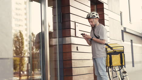 food delivery man wearing thermal backpack calls the entry phone of a building to make a delivery