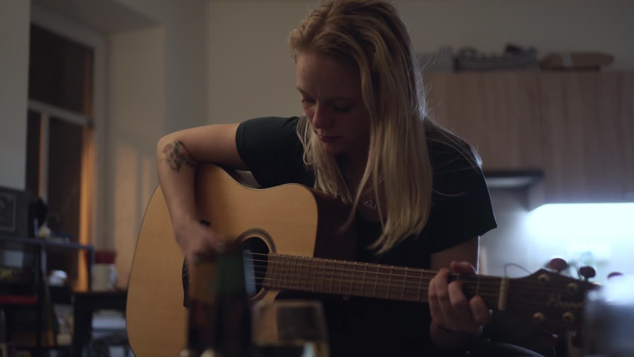 Smuk blond pige spiller guitar hjemme i køkkenet til en husfest