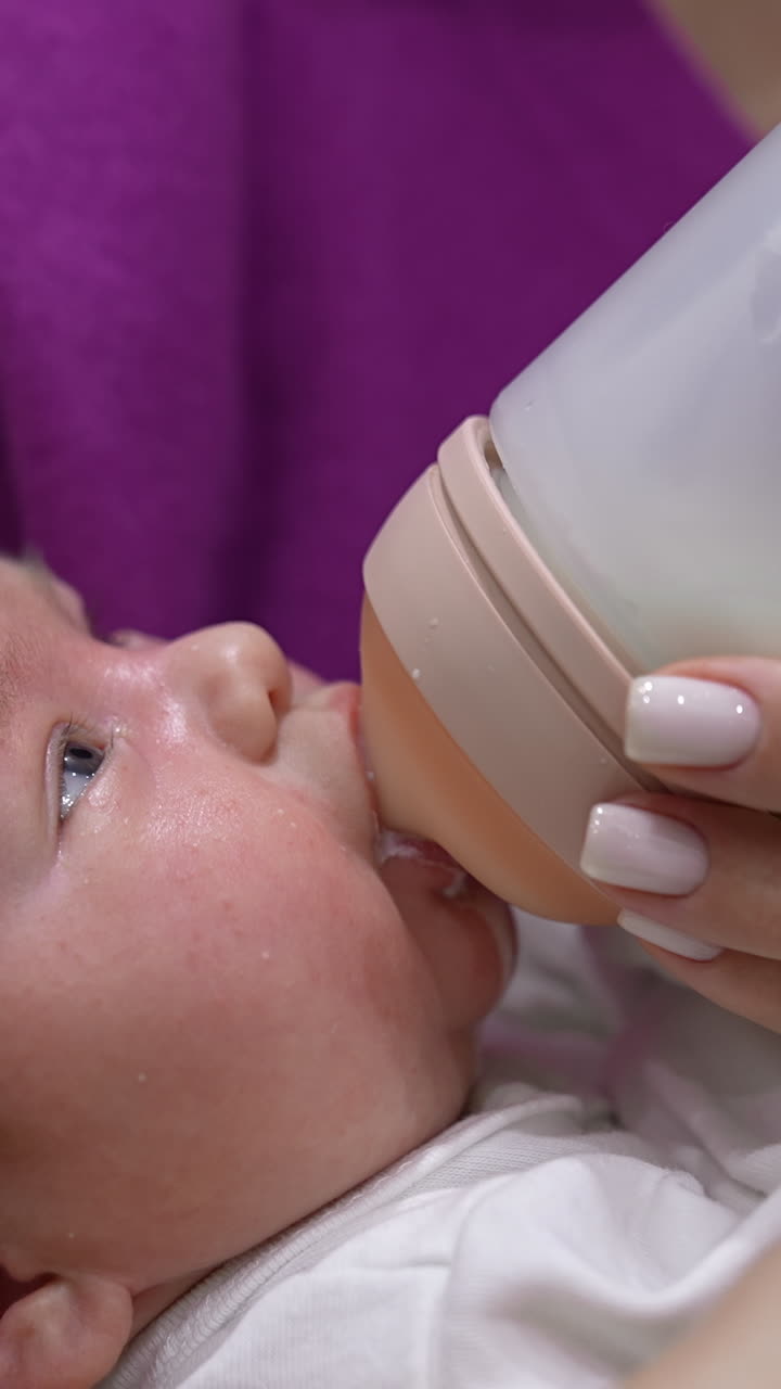 Little infant baby lying on mother's hands. Tiny baby suckling milk from the plastic bottle. Close up shot. Vertical video