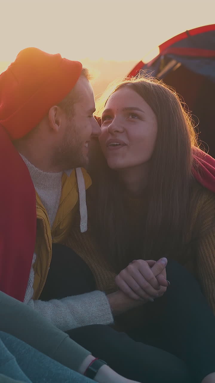 positive young hikers spend time in camp with tent and bonfire on meadow in warm autumn evening against sunset closeup