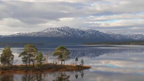 Forest-Island-In-Swedish-Lake-With-Snowcapped-Alpine-Mountains-In-The-Background