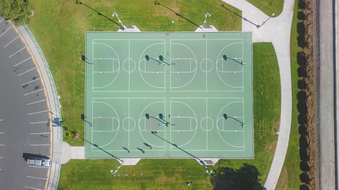 Time lapse con drone con vista dall'alto di persone che si allenano e giocano su un campo da basket in un parco della California meridionale; si muovono in una luminosa giornata di sole, circondate da una vegetazione lussureggiante all'aperto, mostrando la gioia dell'esercizio