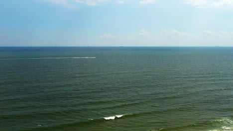 Luftaufnahme-über-Dem-Meer-In-Long-Beach,-New-York,-Während-Ein-Schnelles-Boot-In-Der-Ferne-Nach-Rechts-Davonfährt