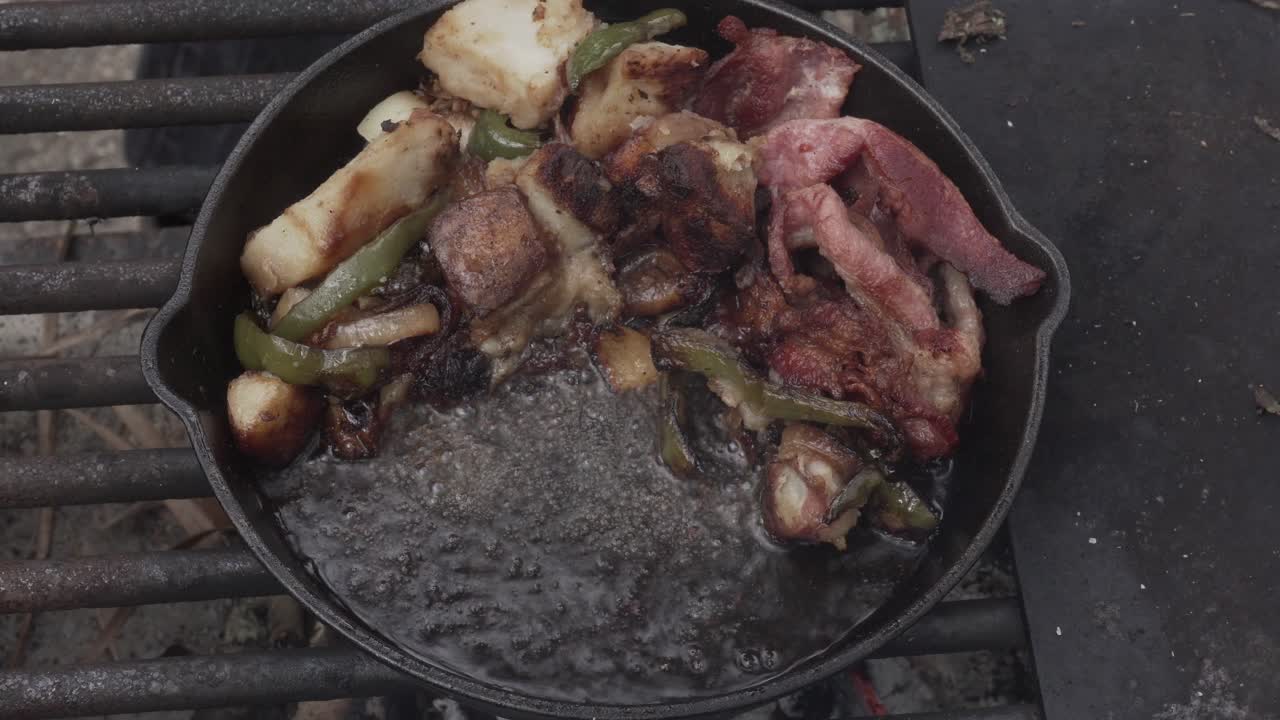 egg, bacon, potatoes, green peppers, onions cooking in a cast iron skillet outdoors at a campground in 4k 29.97p