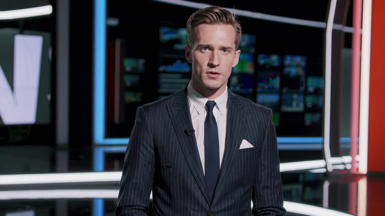 A news anchor in a suit delivers a report in a modern studio. The video uses a medium shot