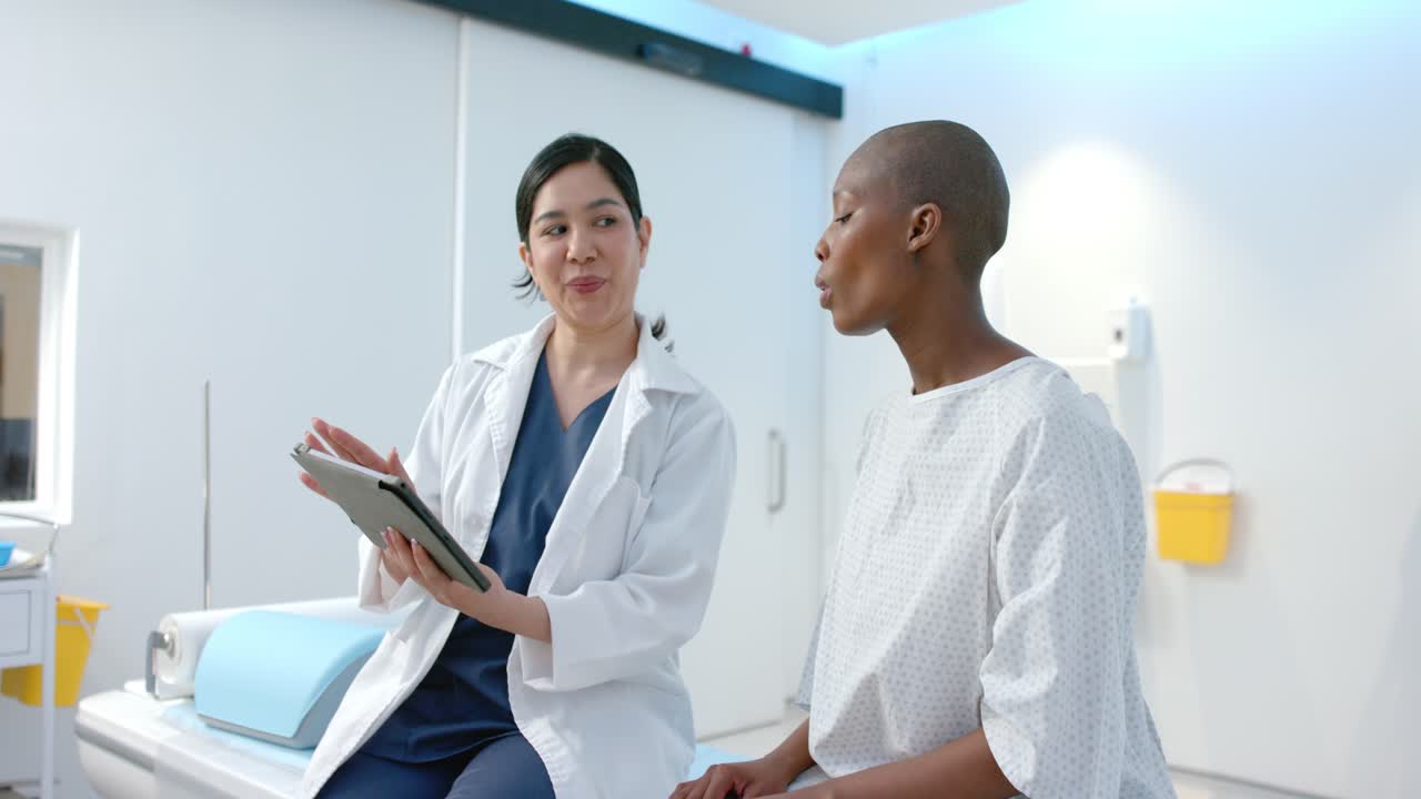 Asian clinician in lab coat showing tablet, reviewing scan in clinic while patient listening