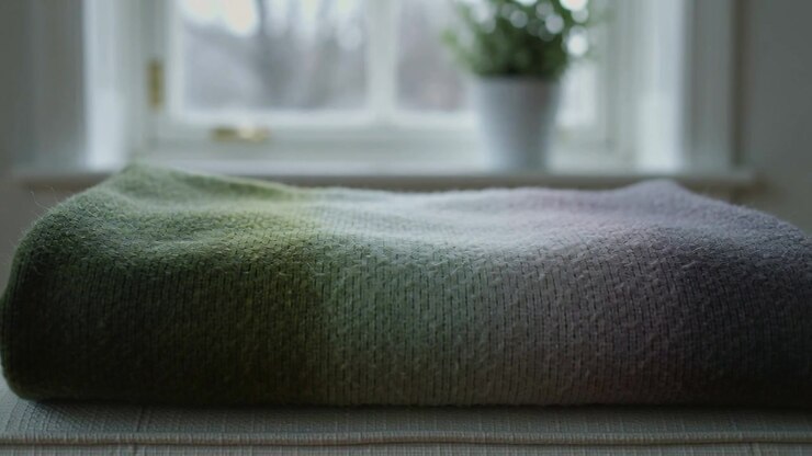 Luce solare che si sposta, coperta in maglia piegata che rivela una trama sottile sul davanzale, con una pianta in vaso