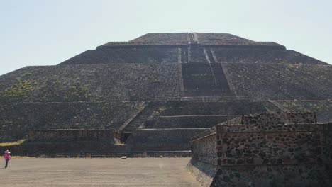 a tracking shot of the pyramid of the sun in the archaeological zone of teotihuacan in mexico, with some tourists walking around it on a clear and sunny day