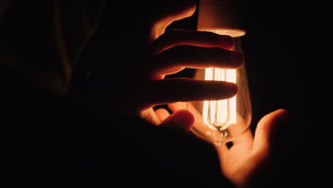 back view of man warms his hands near a light bulb in the dark