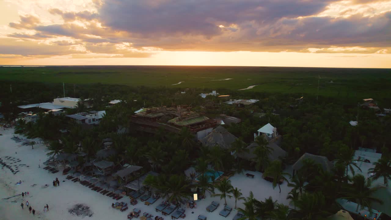 vista aérea de órbita lenta de cabañas de playa y resorts en la playa de akiin en tulum con cielos naranjas al atardecer en el fondo