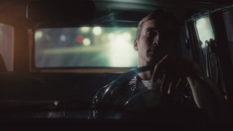 relaxed man driving retro car through city at night