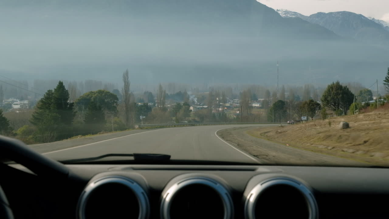 Parabrezza di un'auto che guida su un'autostrada circondata da montagne.