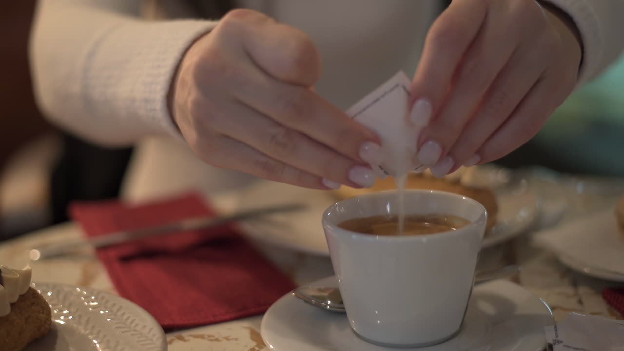 Close up of a woman pouring sugar into her coffee at a cafe