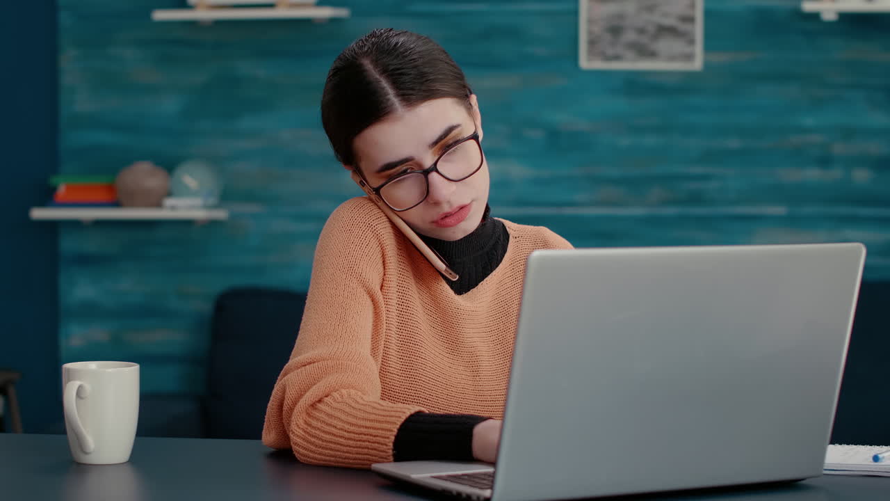 Young woman talking on phone call and using laptop at home desk