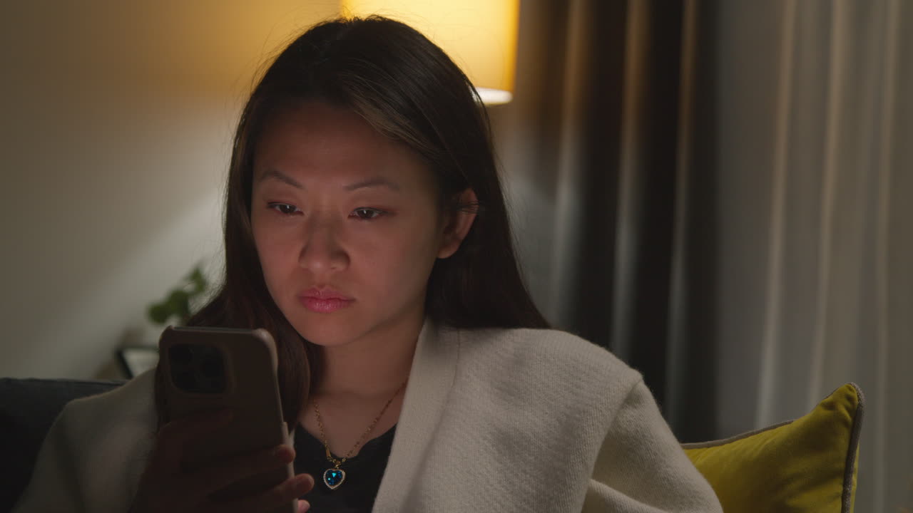 집에서 저녁을 보내고 소파에 앉아 휴대전화를 들고 인터넷이나 소셜 미디어를 스크롤하는 여성의 클로즈업 2