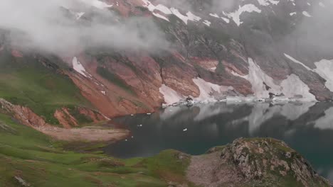 Drone-captures-an-aerial-shot-of-the-beautiful-and-green-Patlian-lake-in-Kashmir-which-surrounded-by-mountains,-Pakistan