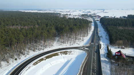 car drives down the highway during sunny day in rakowice, krakow, poland with snow covered woodland on the background