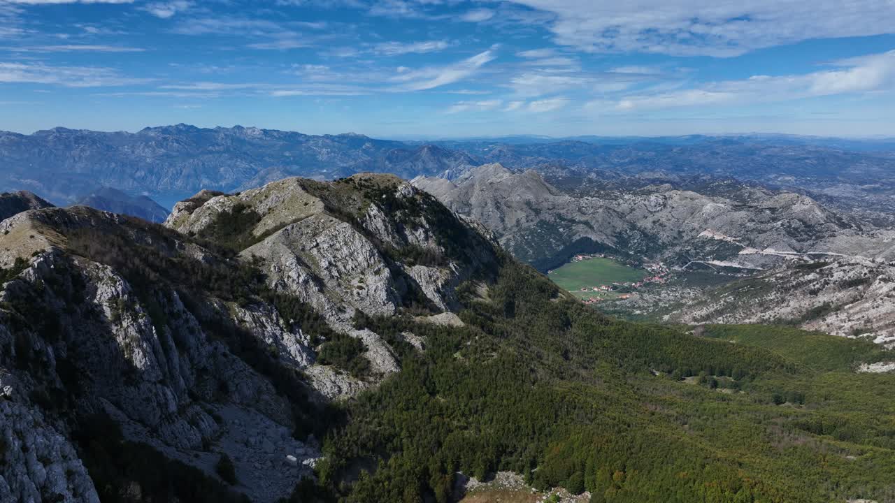 Rocky Lovcen mountain peaks with dense forests and distant valleys, Montenegro. Drone aerial flyover