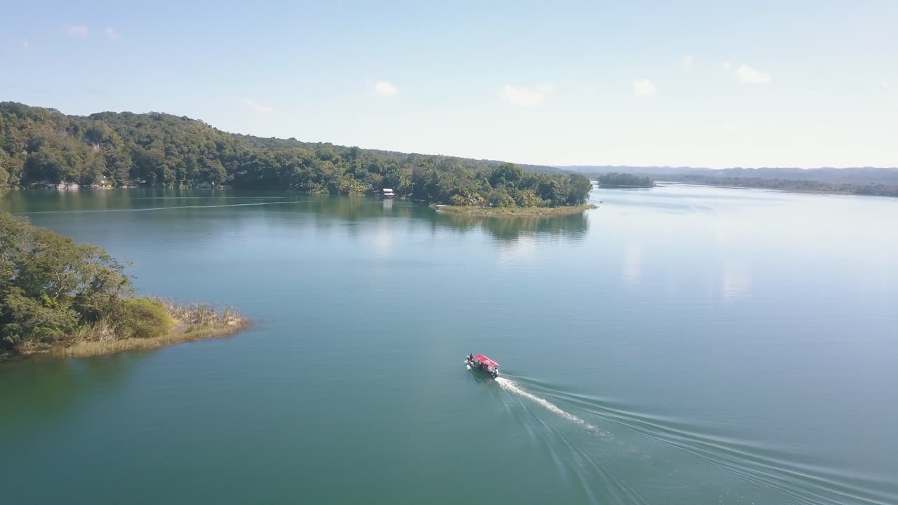 toma aérea de un barco navegando en un lago a una jungla en flores petén, guatemala