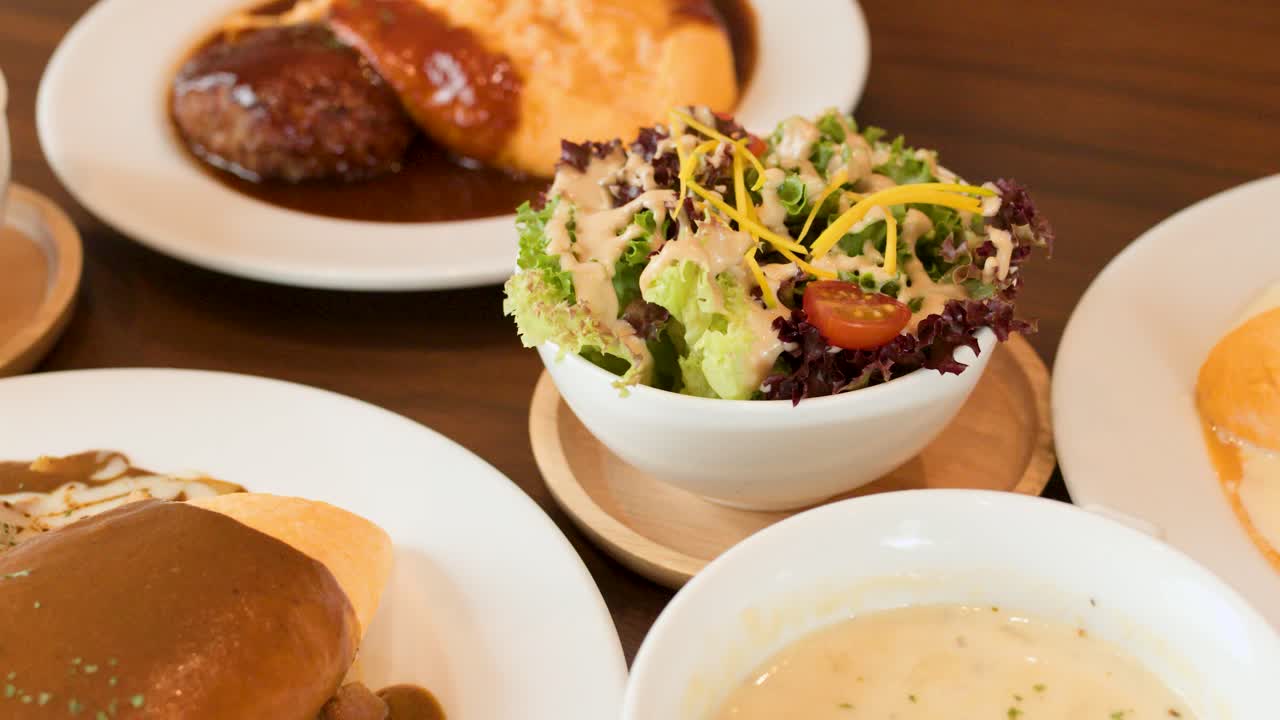 Close-up panning shot of Japanese omelette rice, salad, and soup in bright restaurant lighting