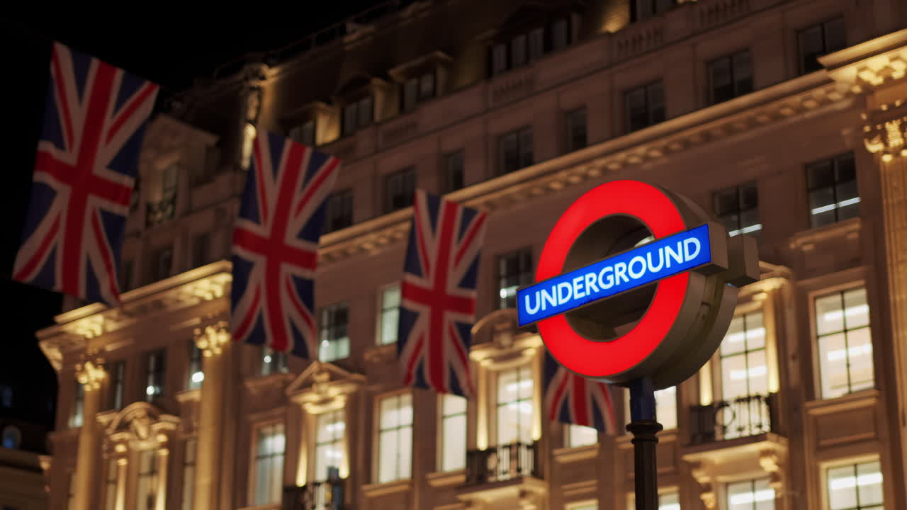 London Underground sign at night with illuminated British flags and classical building in the background in the evening