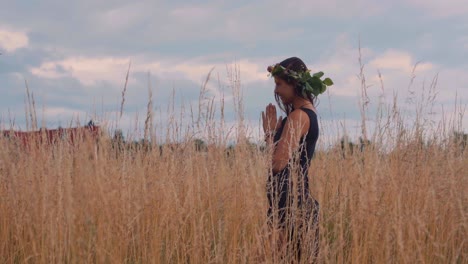 young female with floral wreath on head praying to god in tall countryside grass