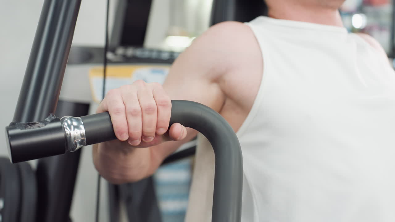 Muscular man seated on cable machine grips handle and pulls weight with controlled motion, muscles contracting under bright gym lighting in modern fitness environment showcasing strength and form