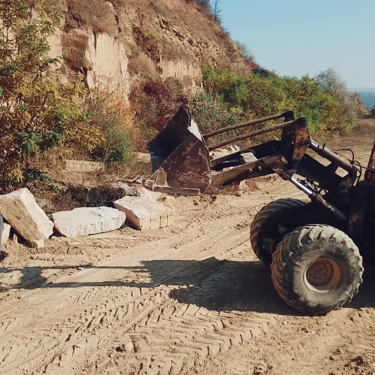 professional yellow bulldozer is working near sand quarry on the background of stones. Camera motion straight