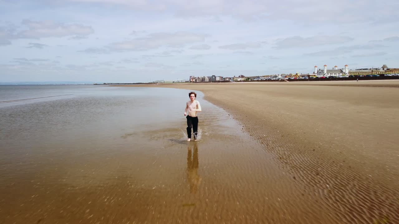 Adult male running along the water&rsquo;s edge making splashes as he goes