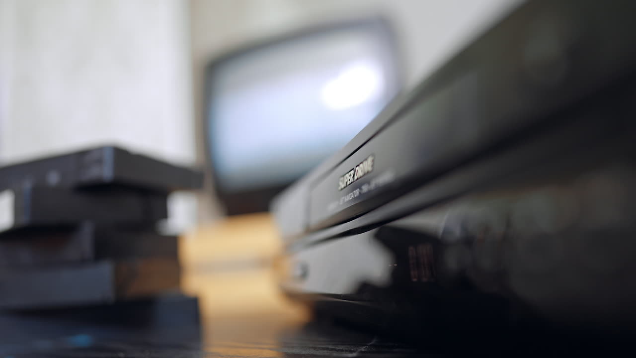 Close hand loading VHS cassette. A close-up of a hand placing a VHS tape into a vintage recorder in a soft-lit room