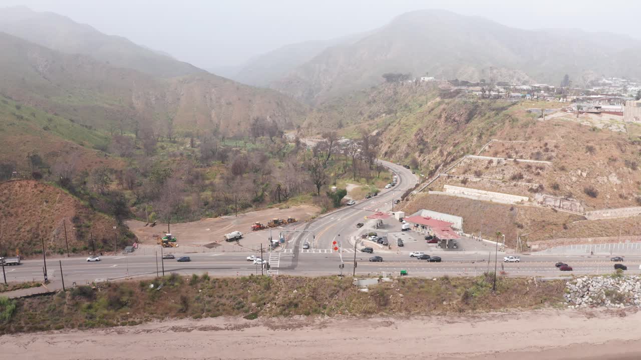 Wide reverse-pullback aerial shot of the intersection of Pacific Coast Highway and Topanga Canyon after the Palisades wildfire in Malibu, California. 4K