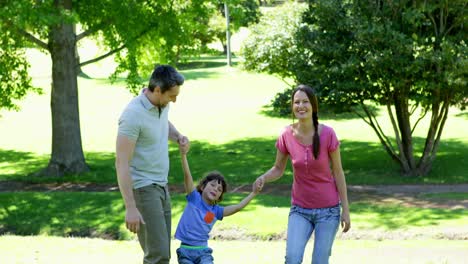 padres felices balanceando a su hijo entre ellos en el parque