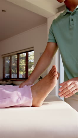 vertical video: physiotherapist massaging senior woman's foot during therapy session in clinic