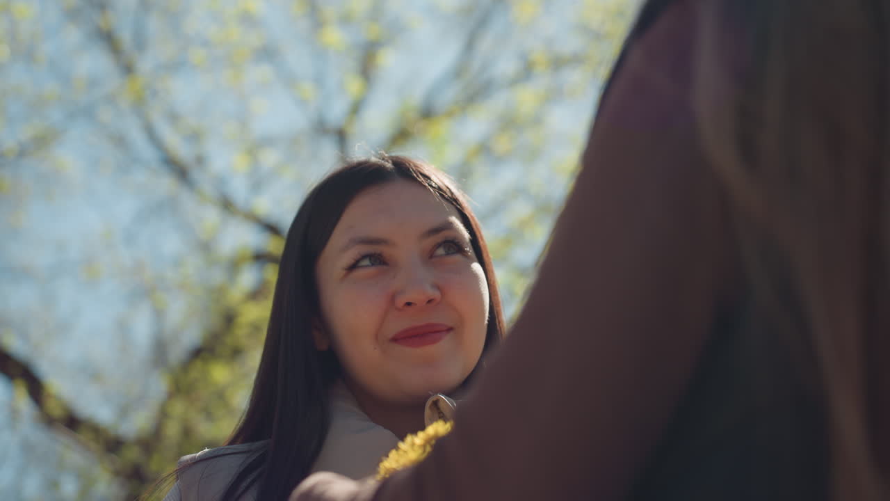 기분 좋은 꽃 교환, 야외에서 꽃을 감상하는 여성, 자연과의 따뜻한 만남과 진심 어린 선물 교환, 봄바람과 햇살이 가득한 공원에서 친구로부터 꽃을 받는 여성