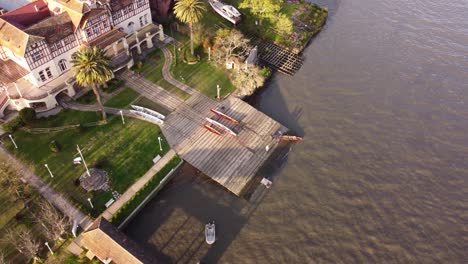 aerial top down shot of people docking rowing boat of tigre river at sunset in buenos aires - arriving wooden dock of river shore
