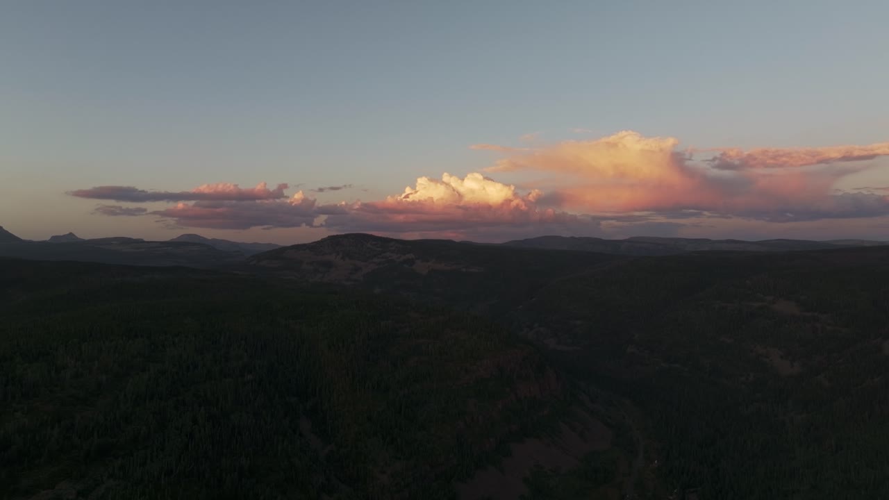 Drone extreme wide shot of the Uinta-Wasatch-Cache National Forest in Utah during a summer sunset, pine trees, Provo River, mountain peaks and clouds rising above the valley