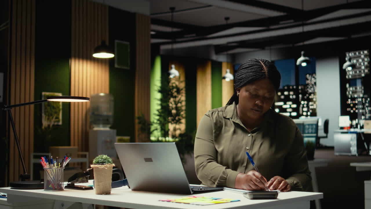 Black analyst documenting essential ideas on paper and reading on laptop
