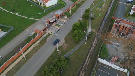 Siguiendo-Un-Auto-Desde-Un-Dron,-El-Auto-Circula-Por-La-Carretera-Al-Lado-De-La-Zona-Residencial-Ciudad-Campestre,-Jamundí,-Valle-Del-Cauca