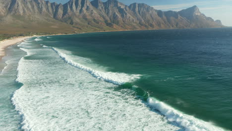 Vista-Aérea-De-Los-Surfistas-Y-El-Océano-Espumoso-En-La-Playa-De-La-Bahía-De-Kogel,-Ciudad-Del-Cabo,-Sudáfrica---Disparo-De-Drones