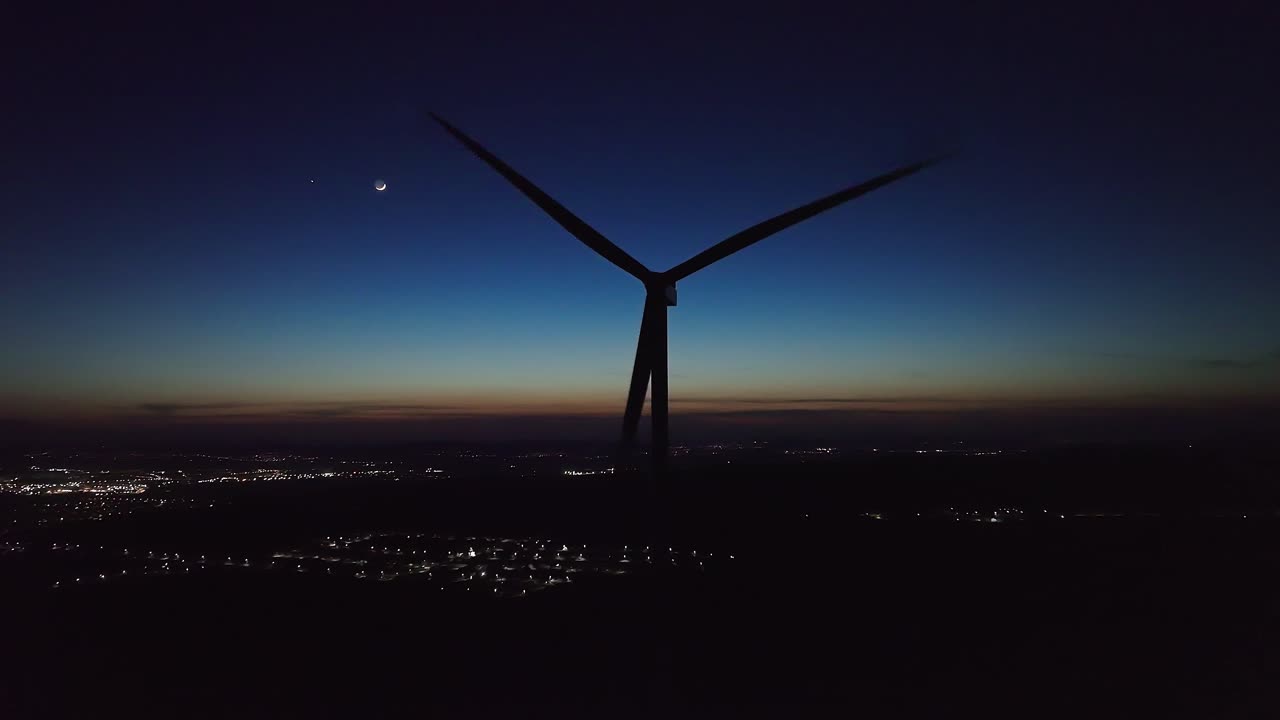 풍력 터빈이 황혼하늘을 향해 서 있고, 도시 불빛이 아래로 박이고 있습니다.