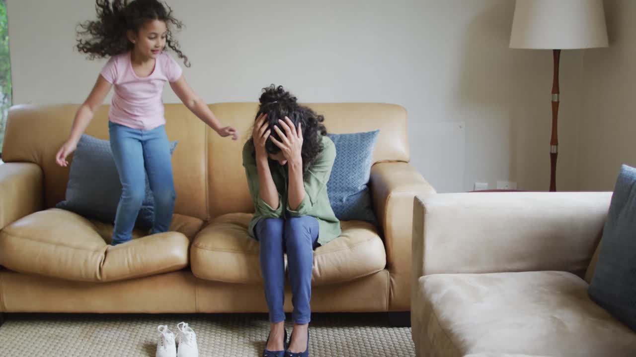 Mixed race daughter jumping on the sofa, mother is stressed