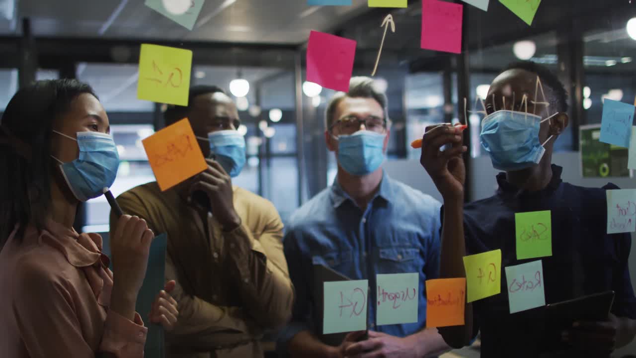 Woman wearing face mask writing with marker pen on on glass board at modern office