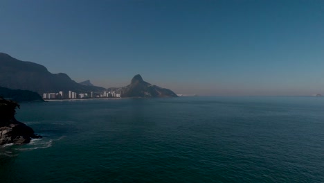 Vista-Aérea-Del-Paisaje-Marino-De-La-Costa-De-Río-De-Janeiro-Con-La-Montaña-Del-Corcovado-Y-Dos-Cimas-Hermanas-Al-Fondo,-Revelando-Una-Pequeña-Isla-En-Primer-Plano