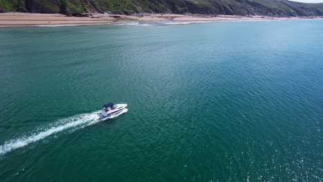 Un-Dron-Aéreo-Sigue-Una-Lancha-Rápida-De-Lujo-A-Lo-Largo-De-La-Costa-De-Cornualles,-Atravesando-Aguas-Turquesas