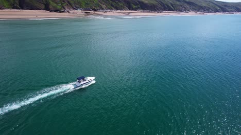 un dron aéreo sigue un barco de velocidad de lujo a lo largo de la costa de cornualles, atravesando aguas turquesas