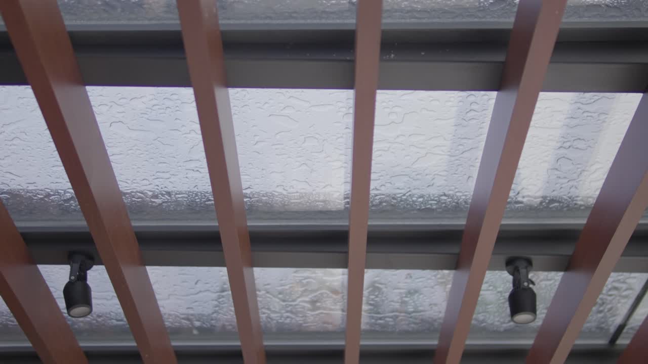 Vista di un soffitto in vetro con travi in legno e faretti neri all'interno.